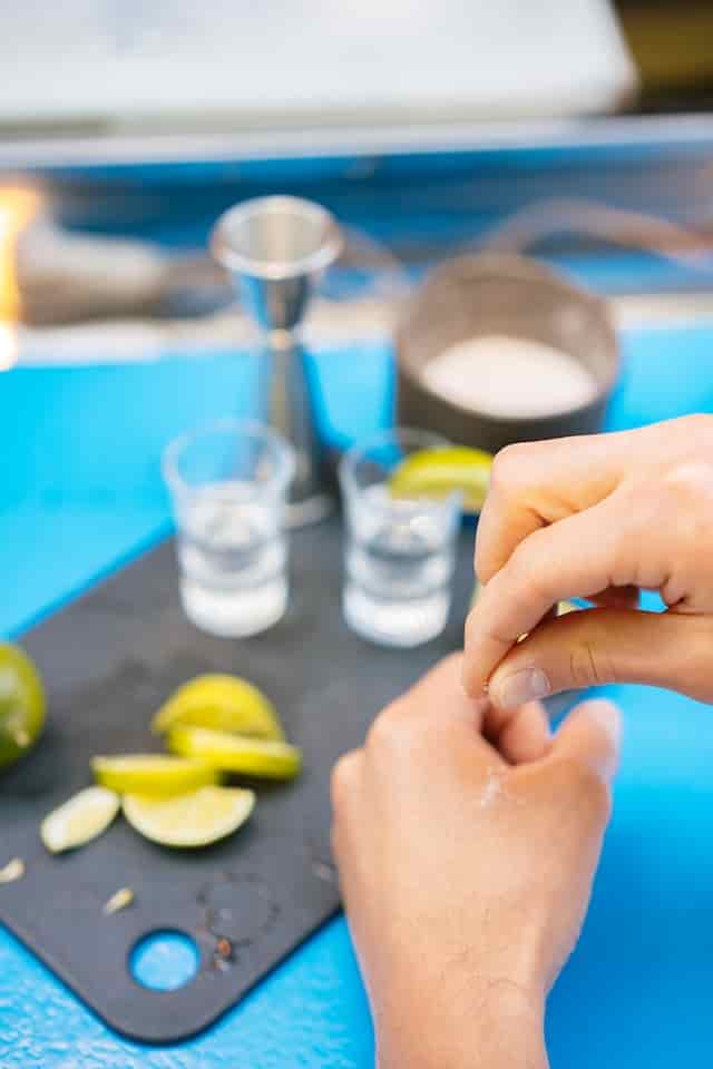 salt on back of hand with limes beside tequila shots on a table